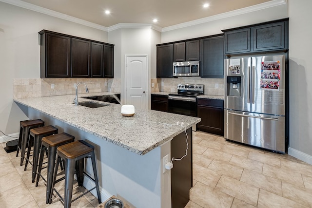kitchen featuring baseboards, a sink, appliances with stainless steel finishes, a kitchen bar, and backsplash
