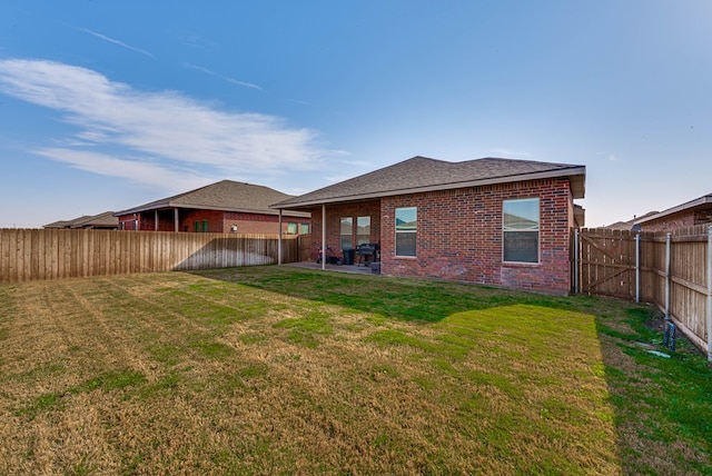 back of house featuring brick siding, a yard, and a fenced backyard