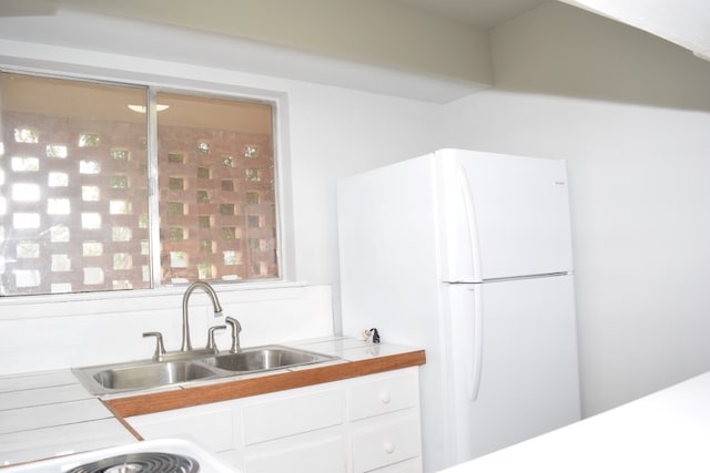 kitchen featuring freestanding refrigerator, a sink, white cabinetry, and tile countertops