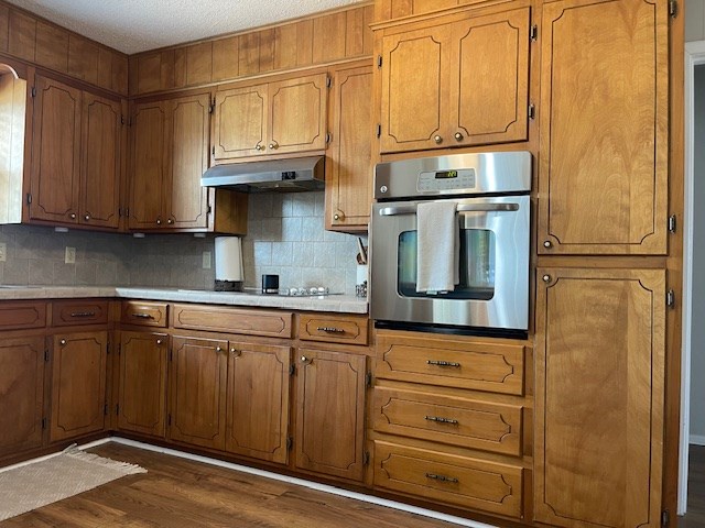 4500 El Paso, Snyder, TX 79549 - kitchen with oven, under cabinet range hood, dark wood finished floors, decorative backsplash, and brown cabinetry