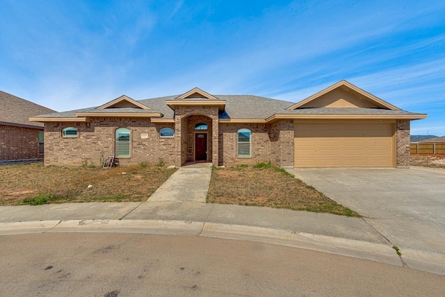 ranch-style house with a shingled roof, an attached garage, brick siding, and concrete driveway