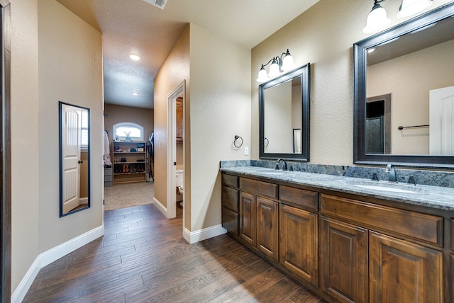 full bathroom featuring baseboards, wood finished floors, double vanity, and a sink