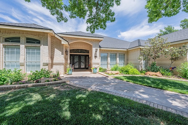 view of exterior entry with brick siding, a lawn, and french doors