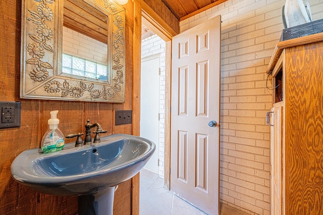 bathroom featuring a sink, tile patterned floors, wood ceiling, and brick wall
