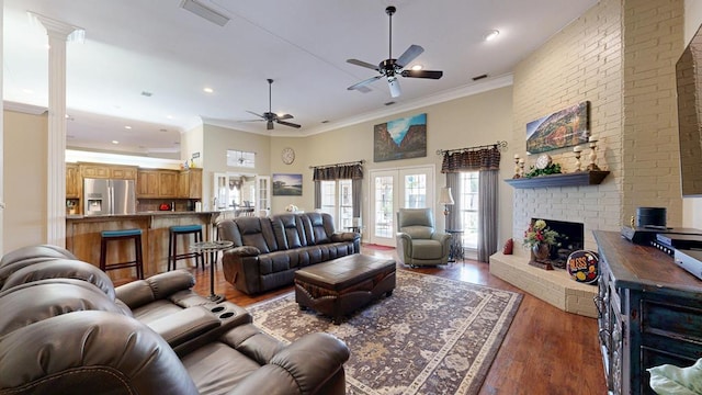living area with a fireplace, a ceiling fan, wood finished floors, visible vents, and ornamental molding