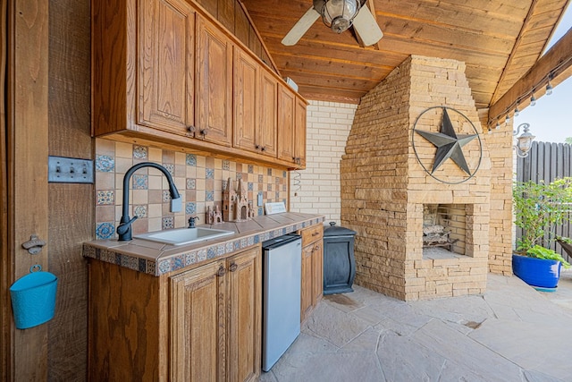 kitchen with stone tile flooring, a ceiling fan, fridge, wooden ceiling, and a sink