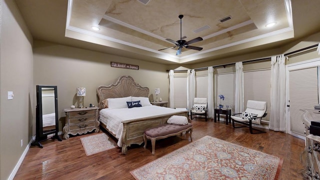 bedroom with baseboards, ornamental molding, a tray ceiling, and wood finished floors