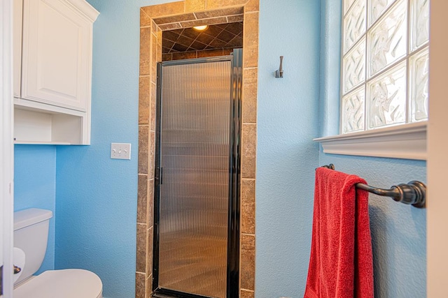 bathroom featuring toilet, a textured wall, and a shower stall