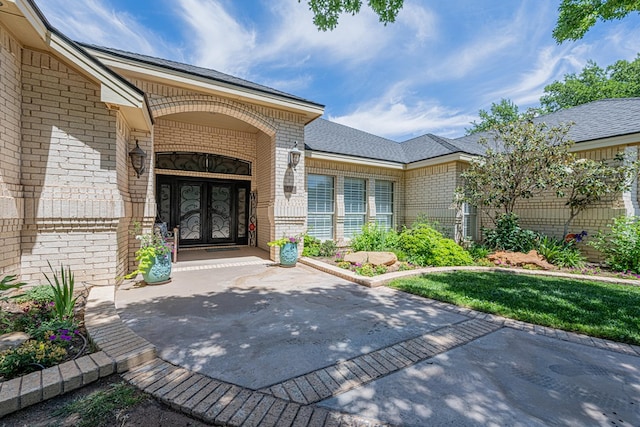 entrance to property with french doors, roof with shingles, and brick siding