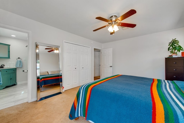 carpeted bedroom with ceiling fan, ensuite bathroom, sink, and a closet