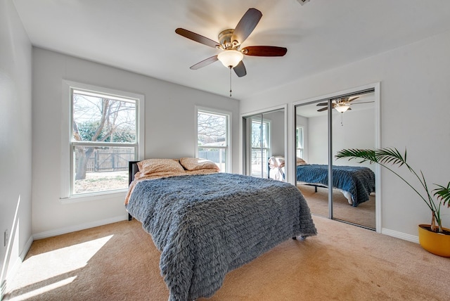 bedroom featuring ceiling fan, light colored carpet, and multiple closets