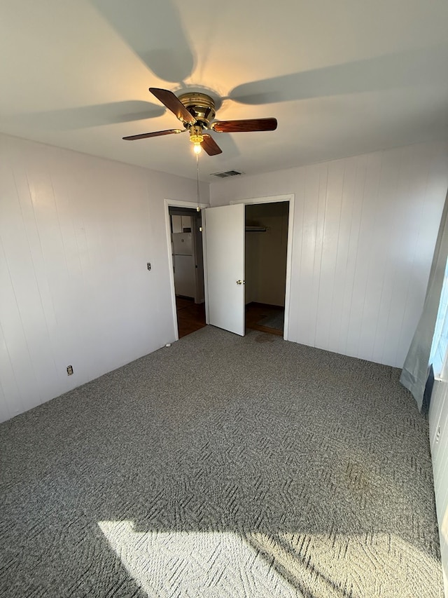 unfurnished bedroom with ceiling fan, wood walls, dark carpet, and a closet