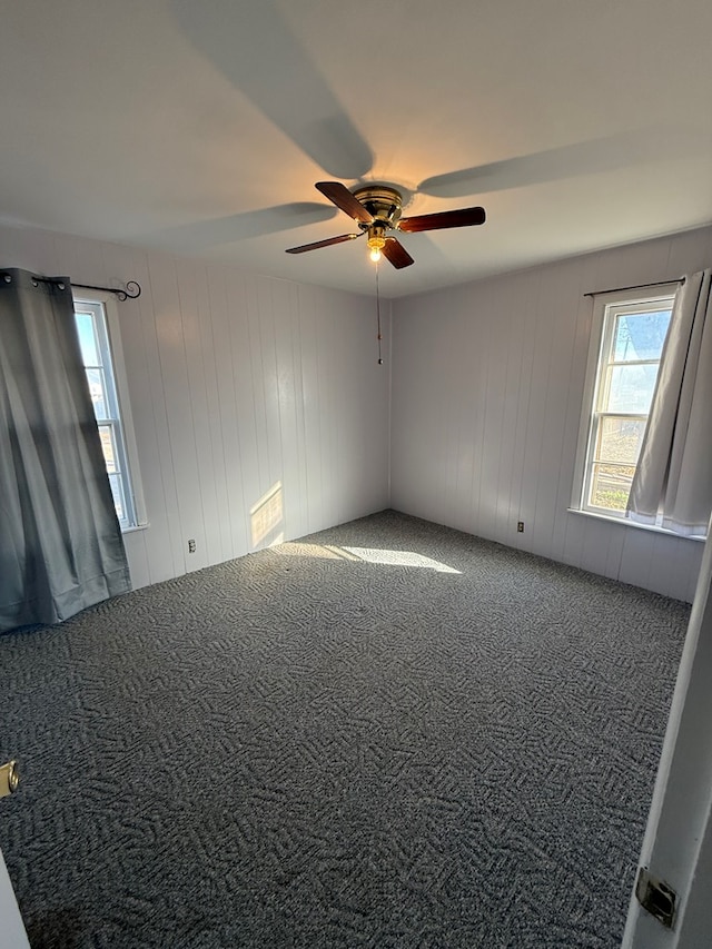 empty room with ceiling fan, wooden walls, and carpet