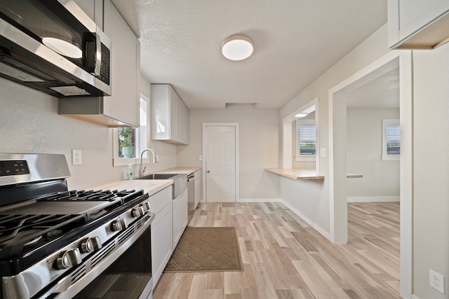 709 E 14th St, Big Spring, TX 79720 - kitchen featuring stainless steel appliances, white cabinetry, light countertops, and light wood-style flooring