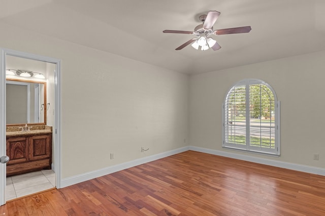 unfurnished bedroom featuring light wood finished floors, baseboards, connected bathroom, a sink, and a ceiling fan