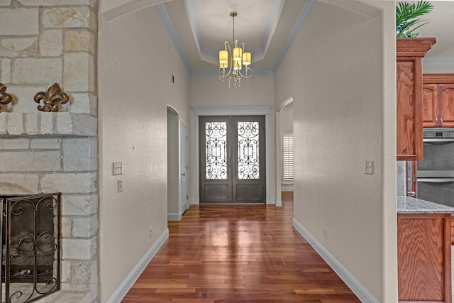 foyer entrance with arched walkways, wood finished floors, a chandelier, a raised ceiling, and ornamental molding