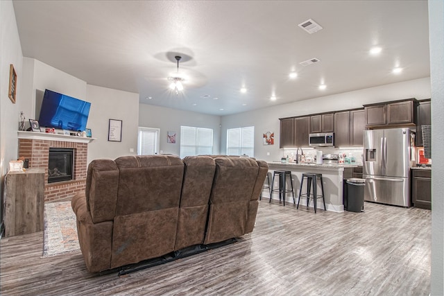 living room with light wood-type flooring, a brick fireplace, and sink