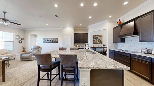 kitchen with premium range hood, a sink, a kitchen breakfast bar, open floor plan, and decorative backsplash