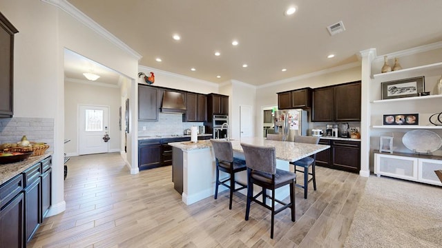 kitchen featuring a breakfast bar area, a center island with sink, visible vents, stainless steel appliances, and wall chimney exhaust hood