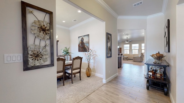 corridor featuring visible vents, baseboards, light wood-style floors, and ornamental molding