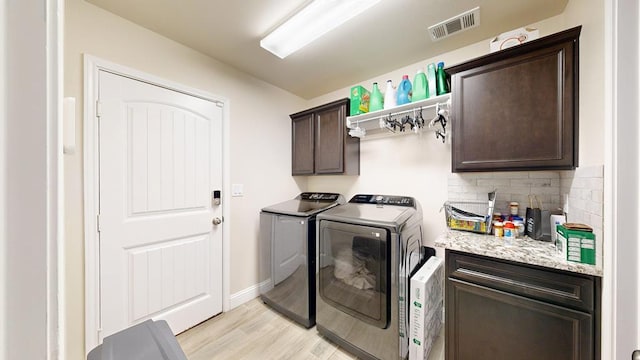 laundry room featuring baseboards, visible vents, cabinet space, light wood-style floors, and washer and clothes dryer