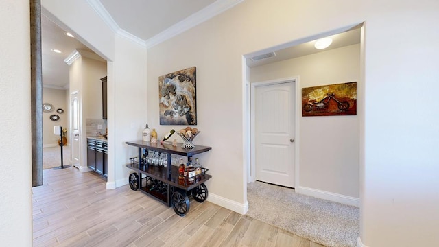 hall featuring visible vents, light wood-style flooring, baseboards, and ornamental molding