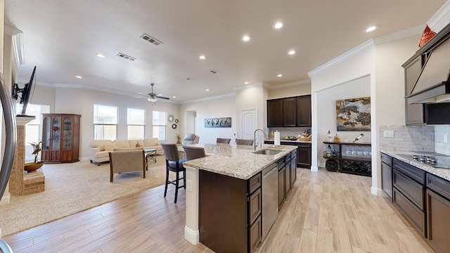 kitchen with visible vents, a kitchen island with sink, a sink, backsplash, and dark brown cabinetry