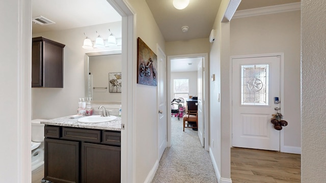 corridor featuring visible vents, light wood-type flooring, a sink, crown molding, and baseboards