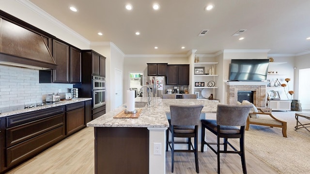 kitchen featuring dark brown cabinets, light stone countertops, custom range hood, a kitchen breakfast bar, and appliances with stainless steel finishes