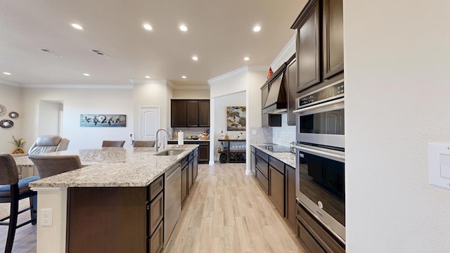 kitchen featuring backsplash, dark brown cabinetry, a large island with sink, stainless steel double oven, and a sink