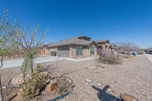 view of front of house featuring an attached garage, fence, stone siding, and driveway