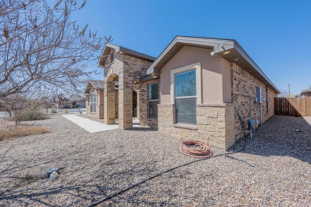 view of side of home featuring stucco siding, stone siding, and fence