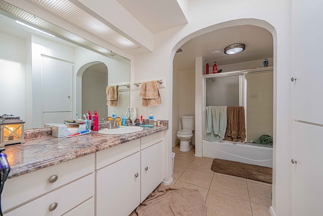 full bathroom with shower / bath combination with glass door, tile patterned flooring, vanity, and toilet