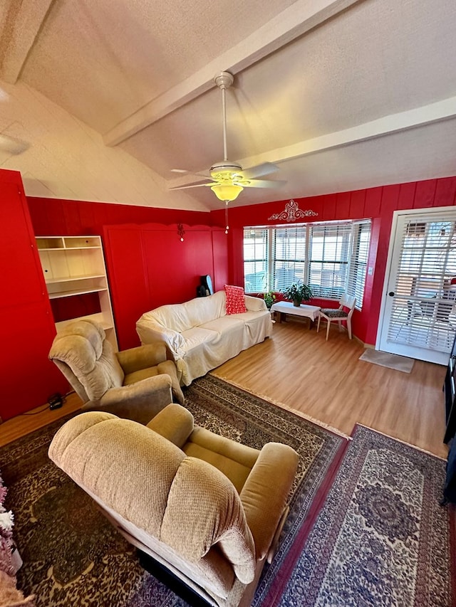 living area featuring a textured ceiling, ceiling fan, wood finished floors, and vaulted ceiling with beams