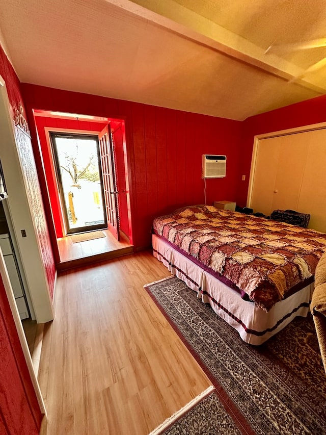 bedroom featuring beamed ceiling, a wall unit AC, and wood finished floors