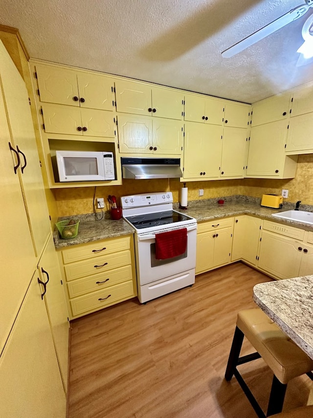 kitchen featuring light wood-style flooring, a sink, a textured ceiling, white appliances, and under cabinet range hood