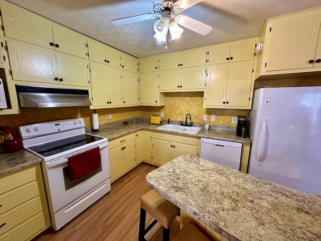 kitchen featuring a textured ceiling, under cabinet range hood, white appliances, a sink, and light wood finished floors