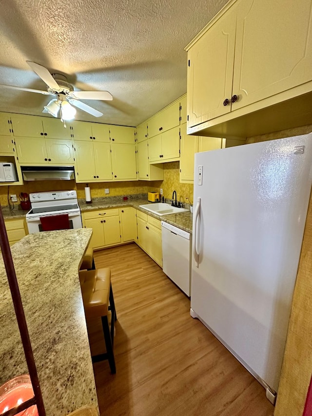 kitchen featuring light wood-style flooring, under cabinet range hood, white appliances, a sink, and a ceiling fan