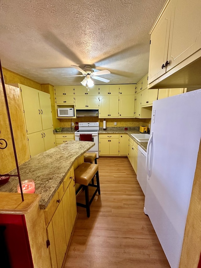 kitchen with ceiling fan, a textured ceiling, light wood-style flooring, under cabinet range hood, and white appliances