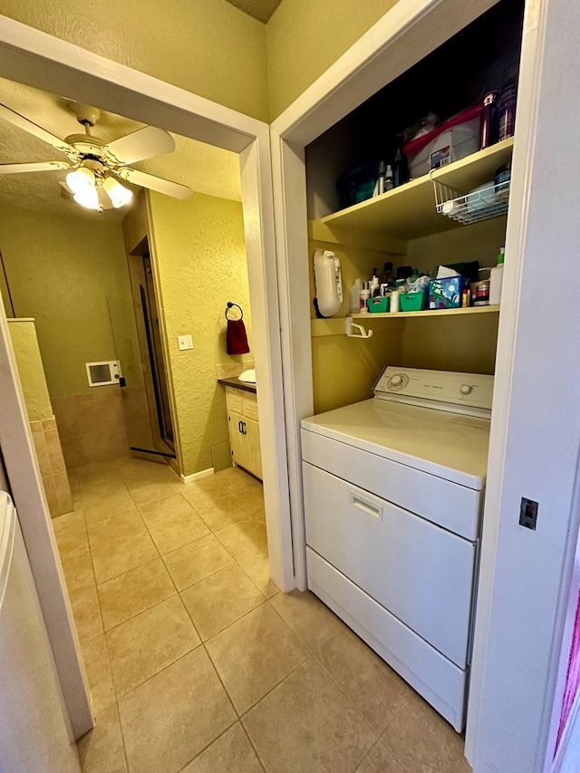 laundry area with laundry area, light tile patterned floors, a ceiling fan, a textured wall, and washer / clothes dryer