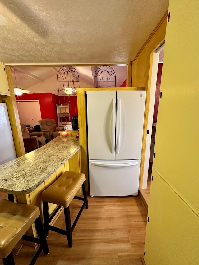 kitchen with a textured ceiling, a peninsula, a kitchen breakfast bar, light wood-style floors, and freestanding refrigerator