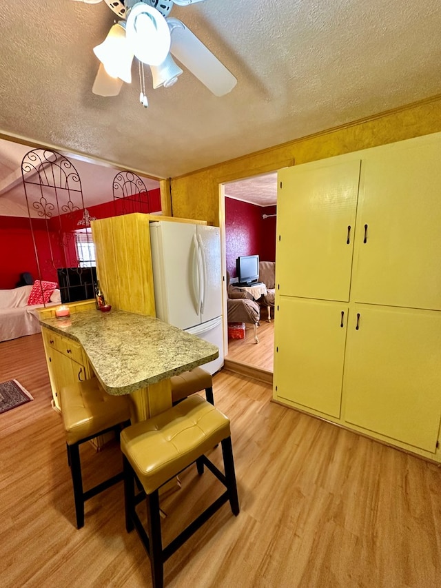 kitchen with a breakfast bar area, light countertops, freestanding refrigerator, a textured ceiling, and light wood-type flooring