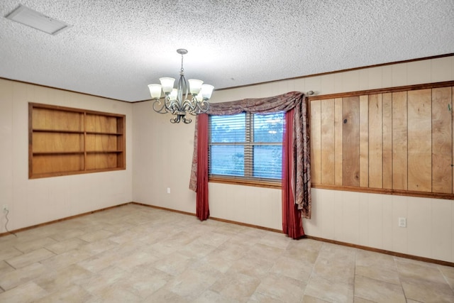 116 W Robinson Rd, Big Spring, TX 79720 - unfurnished room with a textured ceiling, a chandelier, built in shelves, wood walls, and baseboards