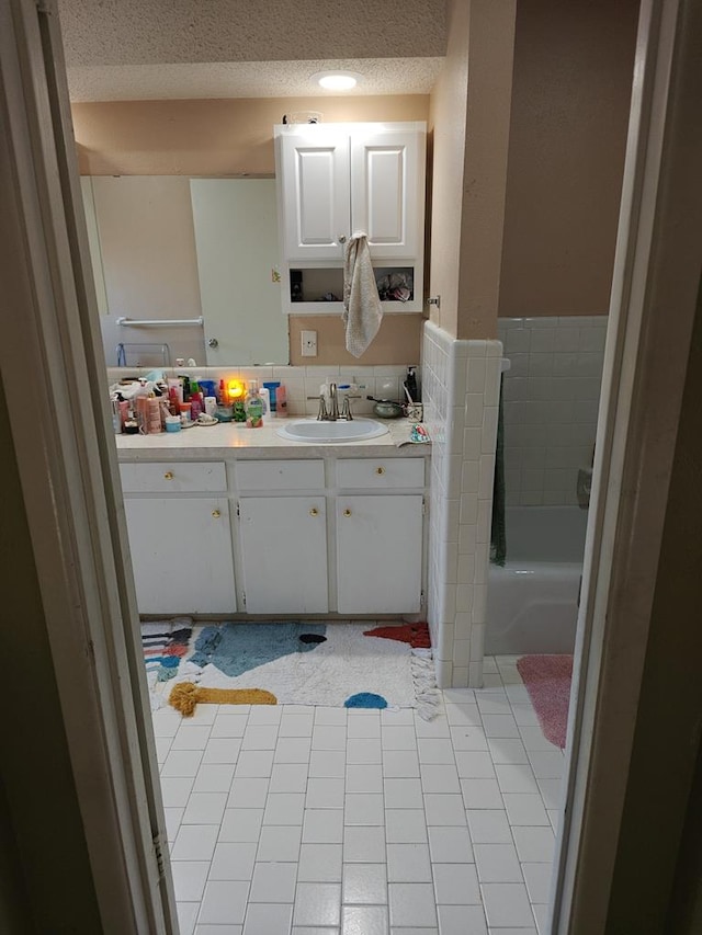 full bath with a tub to relax in, a textured ceiling, and vanity