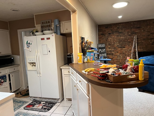 kitchen featuring white refrigerator with ice dispenser, light tile patterned floors, stainless steel microwave, brick wall, and a peninsula