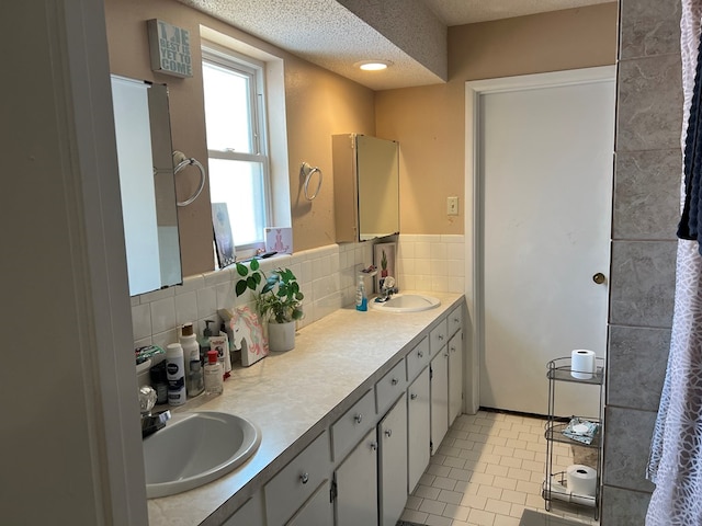 full bath with a textured ceiling, double vanity, tile patterned flooring, and a sink