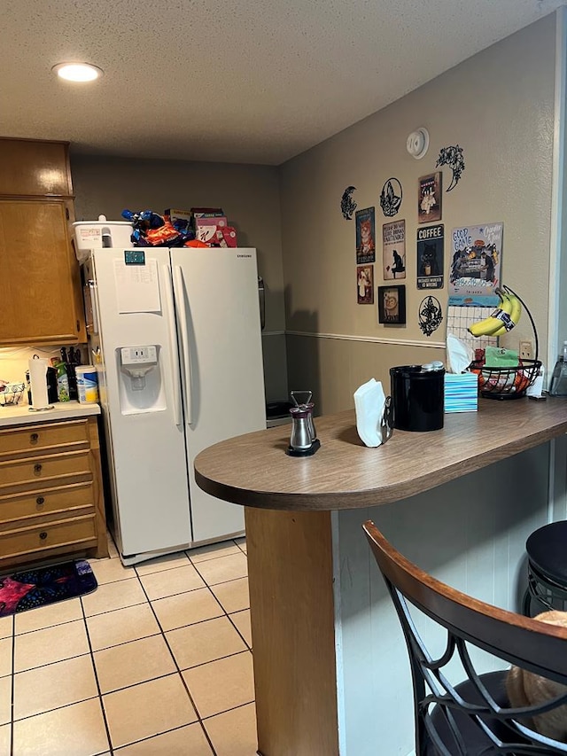 kitchen featuring a breakfast bar, white refrigerator with ice dispenser, light tile patterned floors, a textured ceiling, and a peninsula