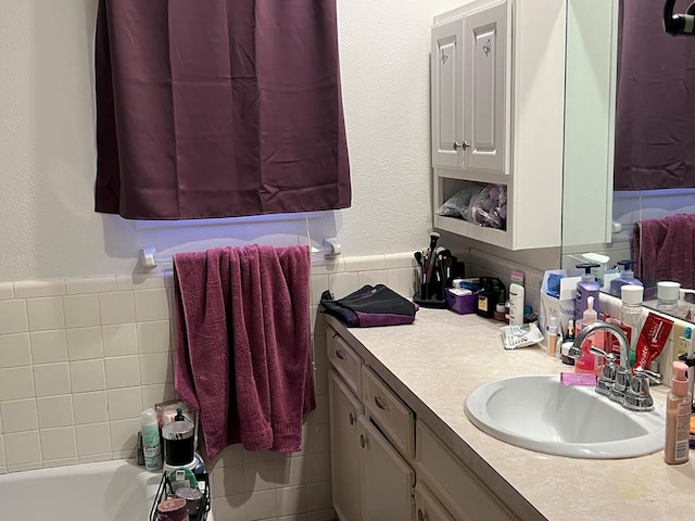 full bath featuring a textured wall, a bathing tub, vanity, and tile walls