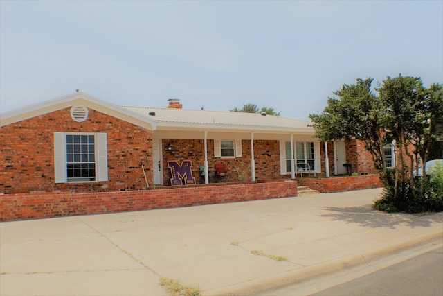 ranch-style home featuring covered porch, brick siding, and a chimney