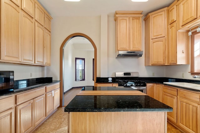 kitchen with light brown cabinets, dark stone counters, sink, gas range, and a kitchen island